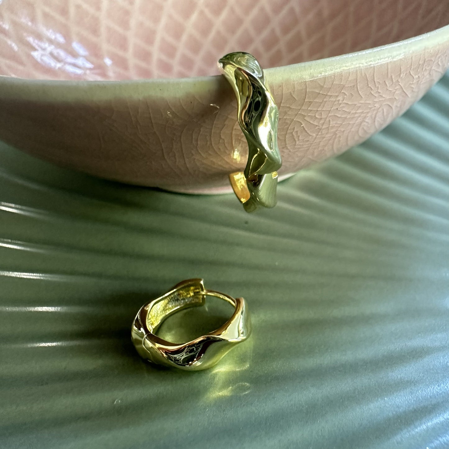 Gold chunky statment earrings on a textured green surface with a pink bowl in the background