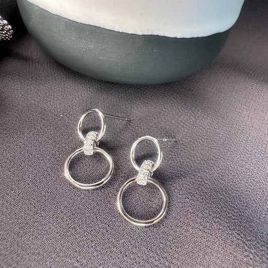 Silver earrings with two interlocking rings on a gray surface