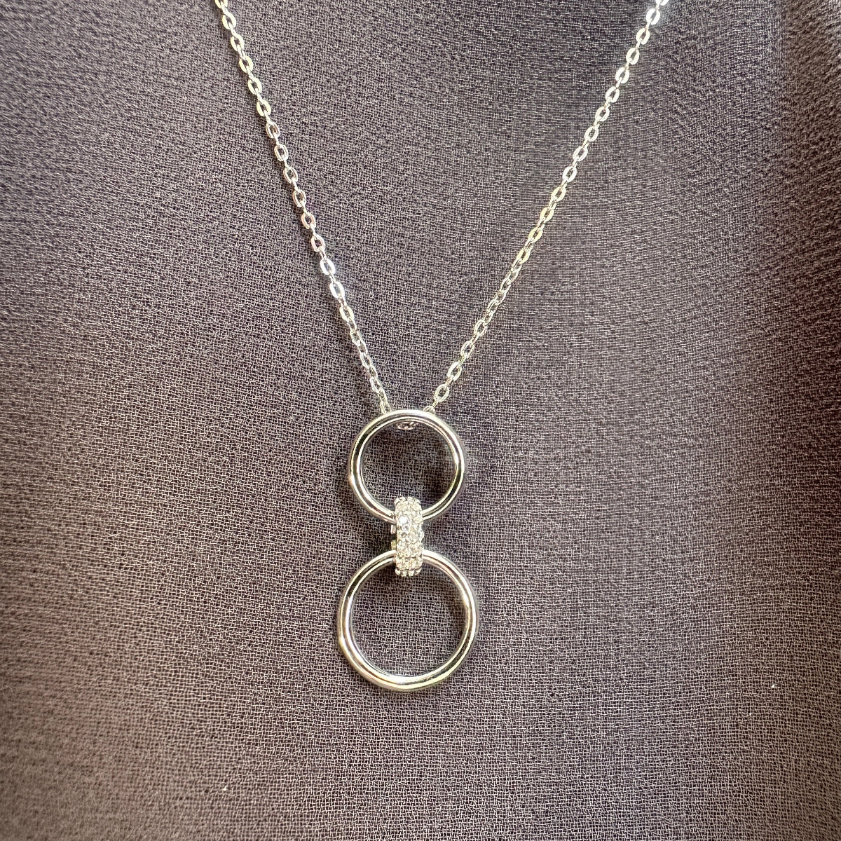 Silver necklace with a double-ring pendant on a textured brown surface