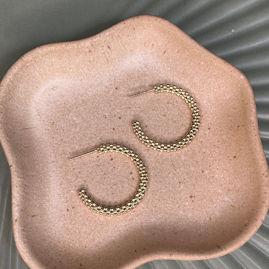 Gold hoop earrings on a textured beige surface