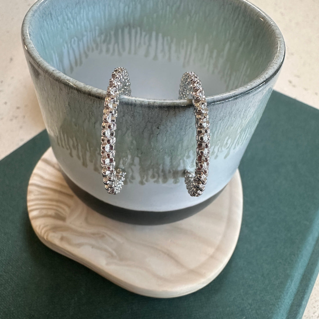 Silver hoop earrings displayed on a ceramic stand with a textured bowl in the background.
