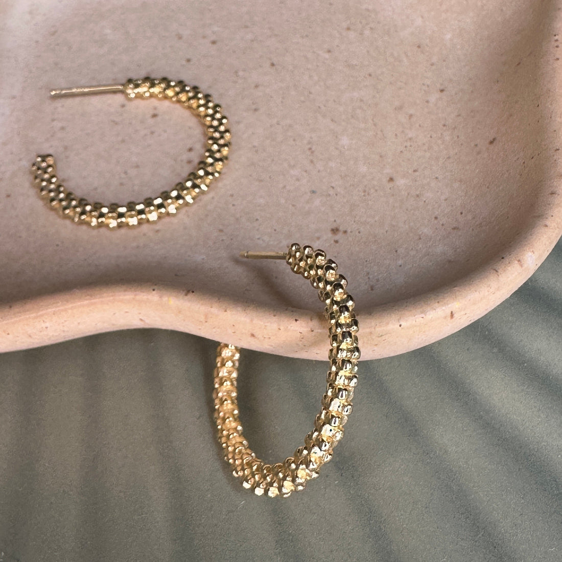 Gold hoop earrings on a textured beige surface