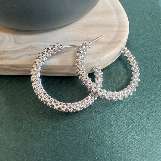 Silver hoop earrings on a green surface with a neutral background