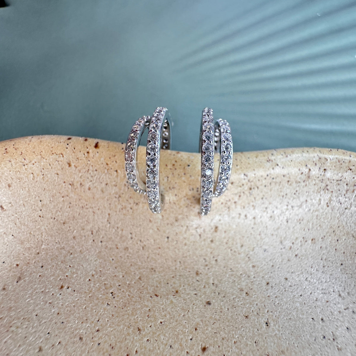 Silver hoop earrings with embedded stones on a textured blue surface