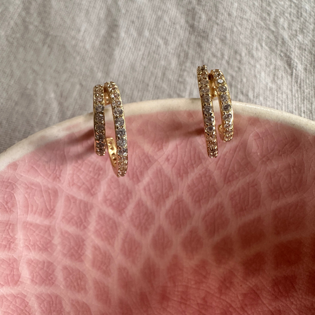 Gold hoop earrings with embedded stones on a textured pink surface