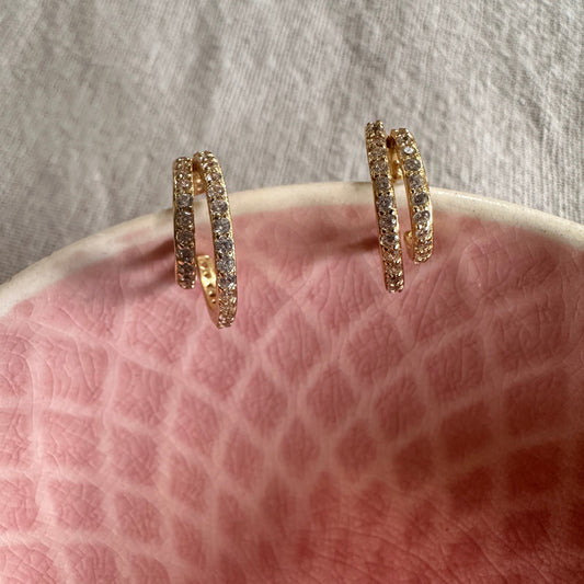 Gold hoop earrings with embedded stones on a textured pink surface