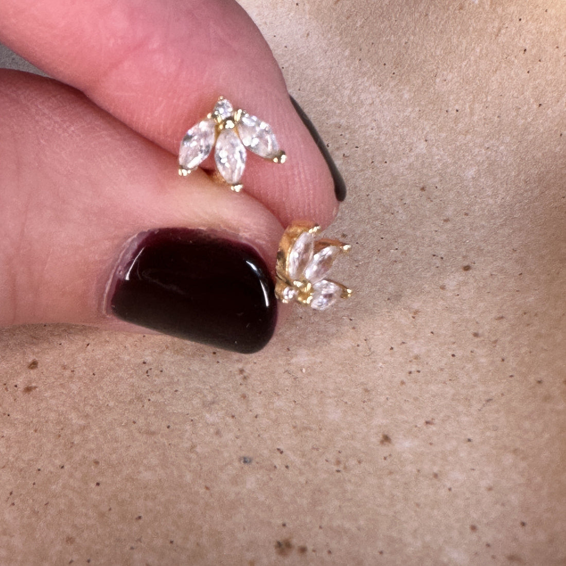 Gold earrings with clear stones held between fingers on a beige background