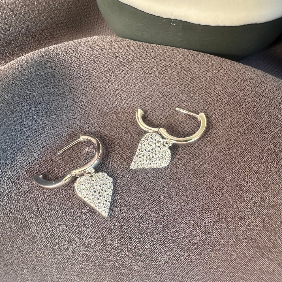 Silver heart-shaped earrings on a textured surface