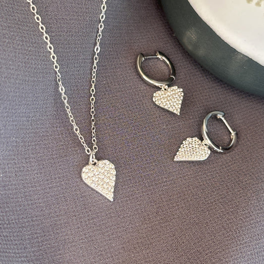 Silver heart-shaped necklace and earrings on a gray surface