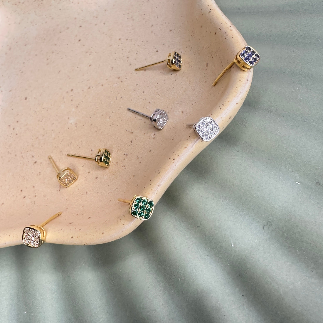 Collection of gold and silver earrings on a textured beige surface.