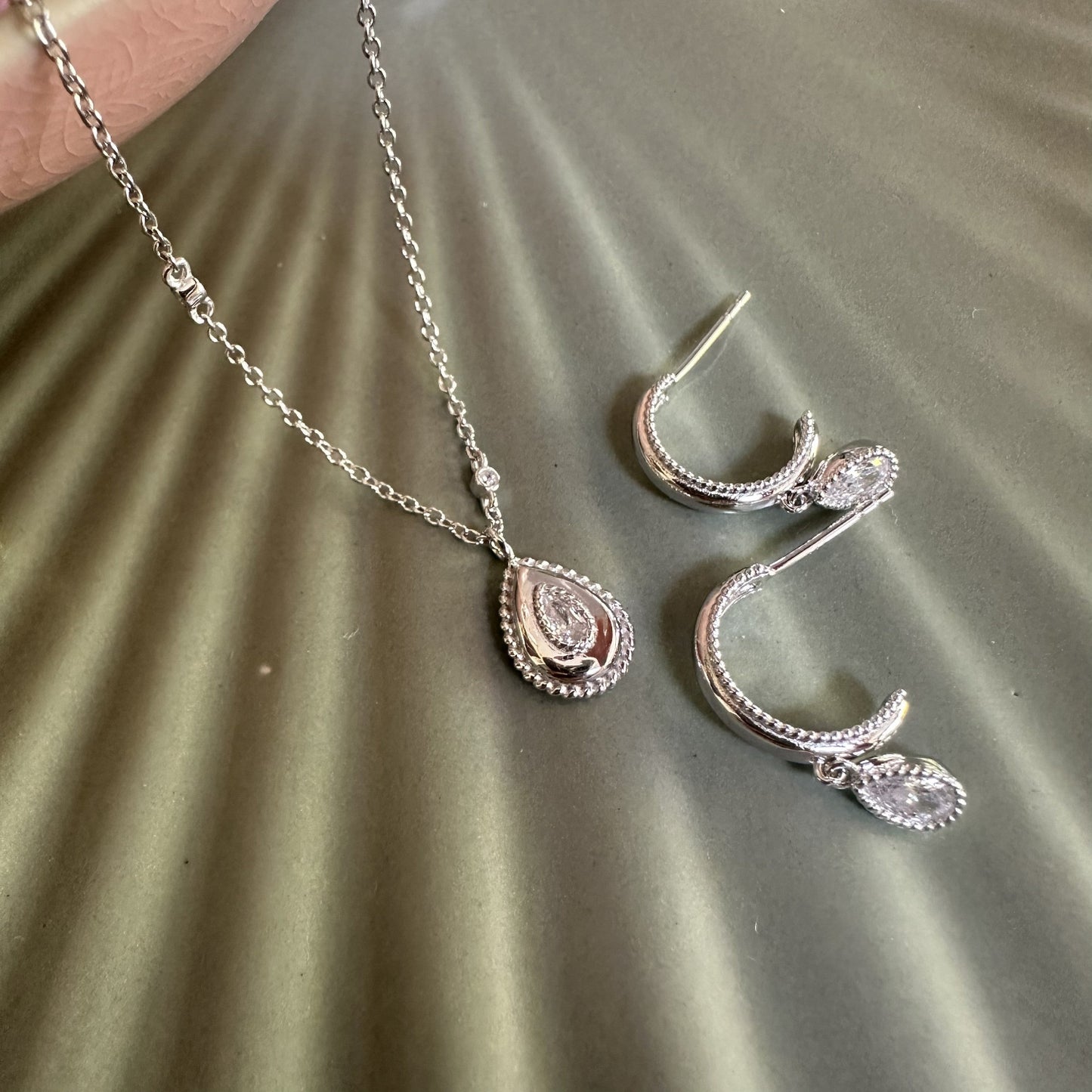 Silver Teardrop Pear Pendant Charm necklace and earrings on a textured surface