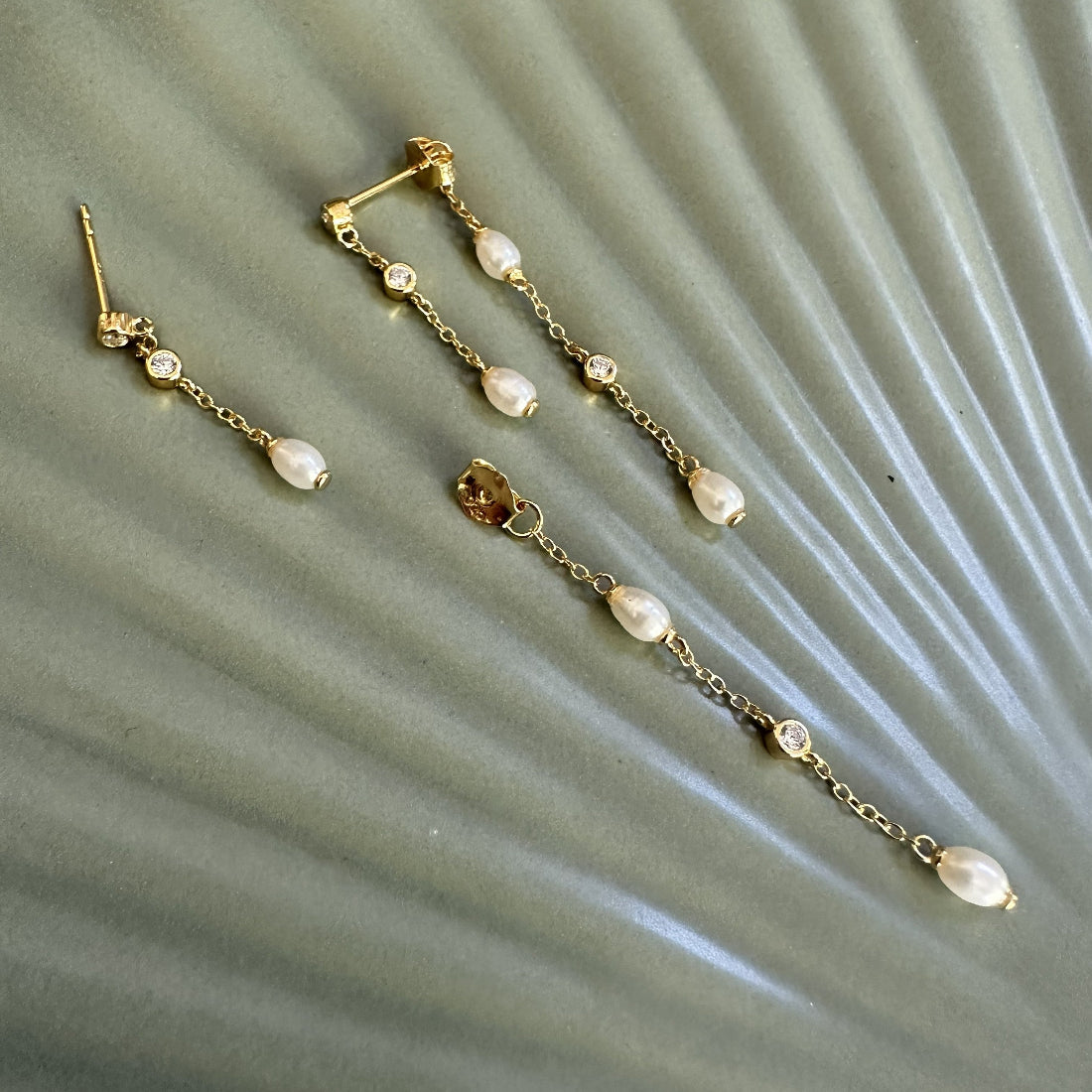 Gold chain earrings with natural freshwater pearls with gemstones on a textured surface