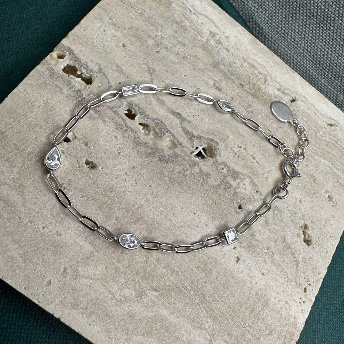 Silver bracelet with different shape gemstones for a modern style design on terazzo tile background
