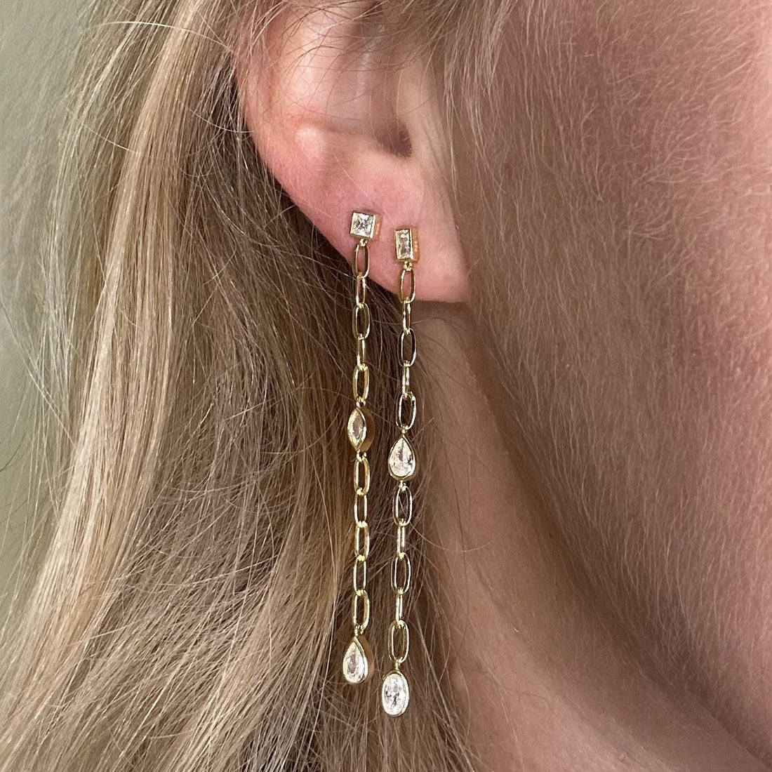 pair of gemstone earrings in asymmetric design featuring different shaped cubic zirconia gemstones.  On model ear