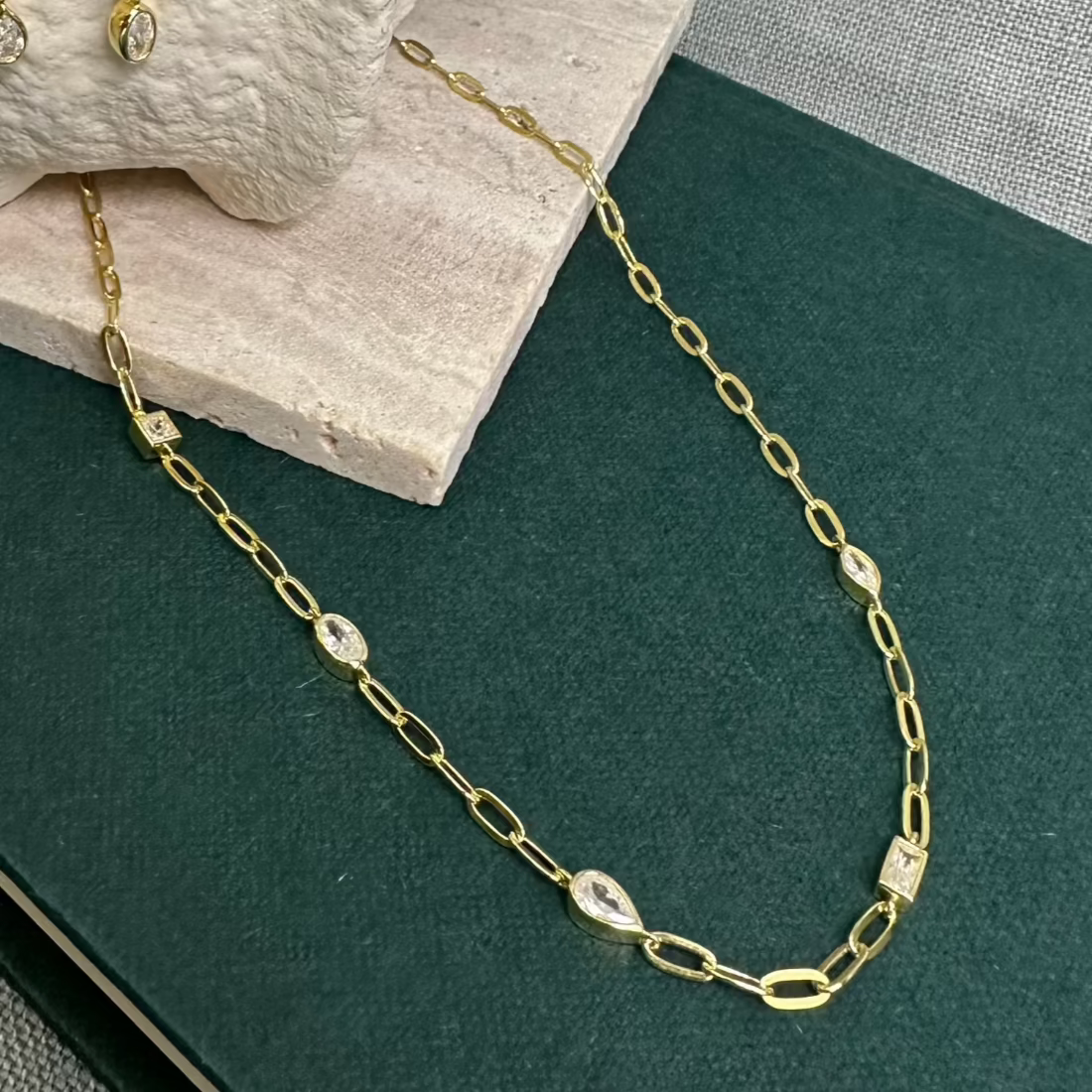 Gold Necklace with different shape  gemstones on green background