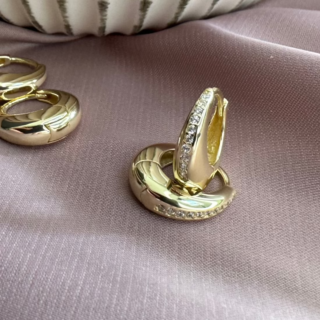 beautiful pair of gold dome shaped earrings with channel set pave gemstones for a modern setting, sat on a pink fabric