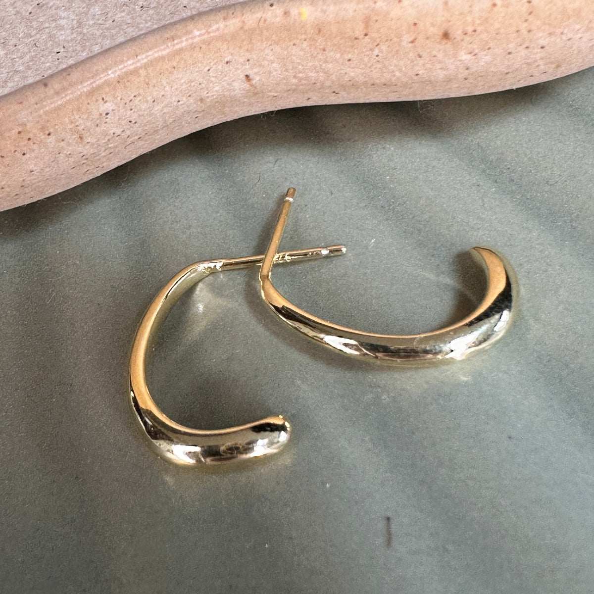 Gold hoop earrings on a gray surface with a beige stone