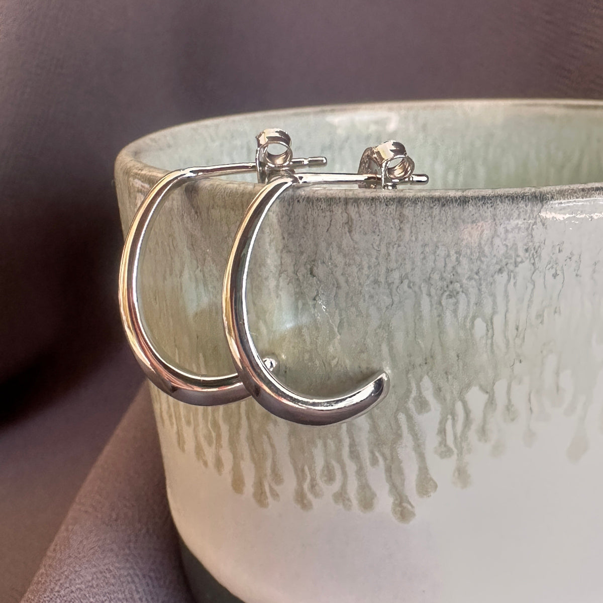 Silver hoop earrings on a textured ceramic surface