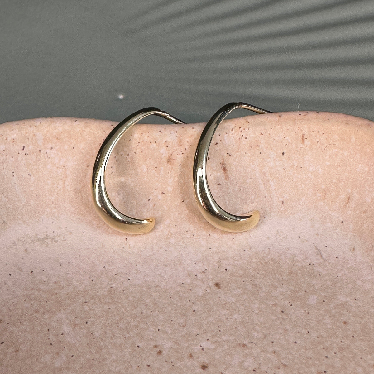 Gold hoop earrings on a beige surface with a gray background