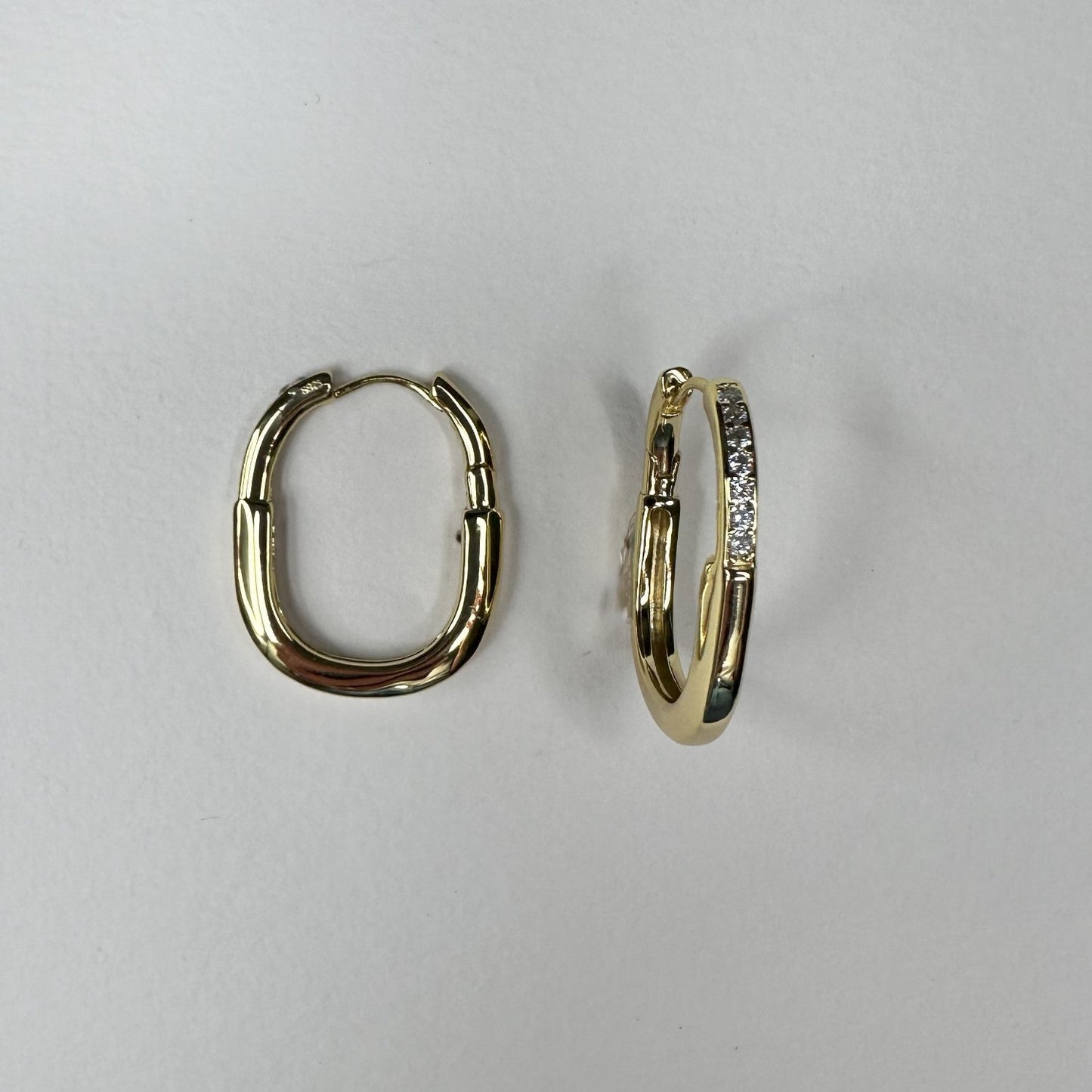 gold oval hoop earrings with gemstones on a white matte plate