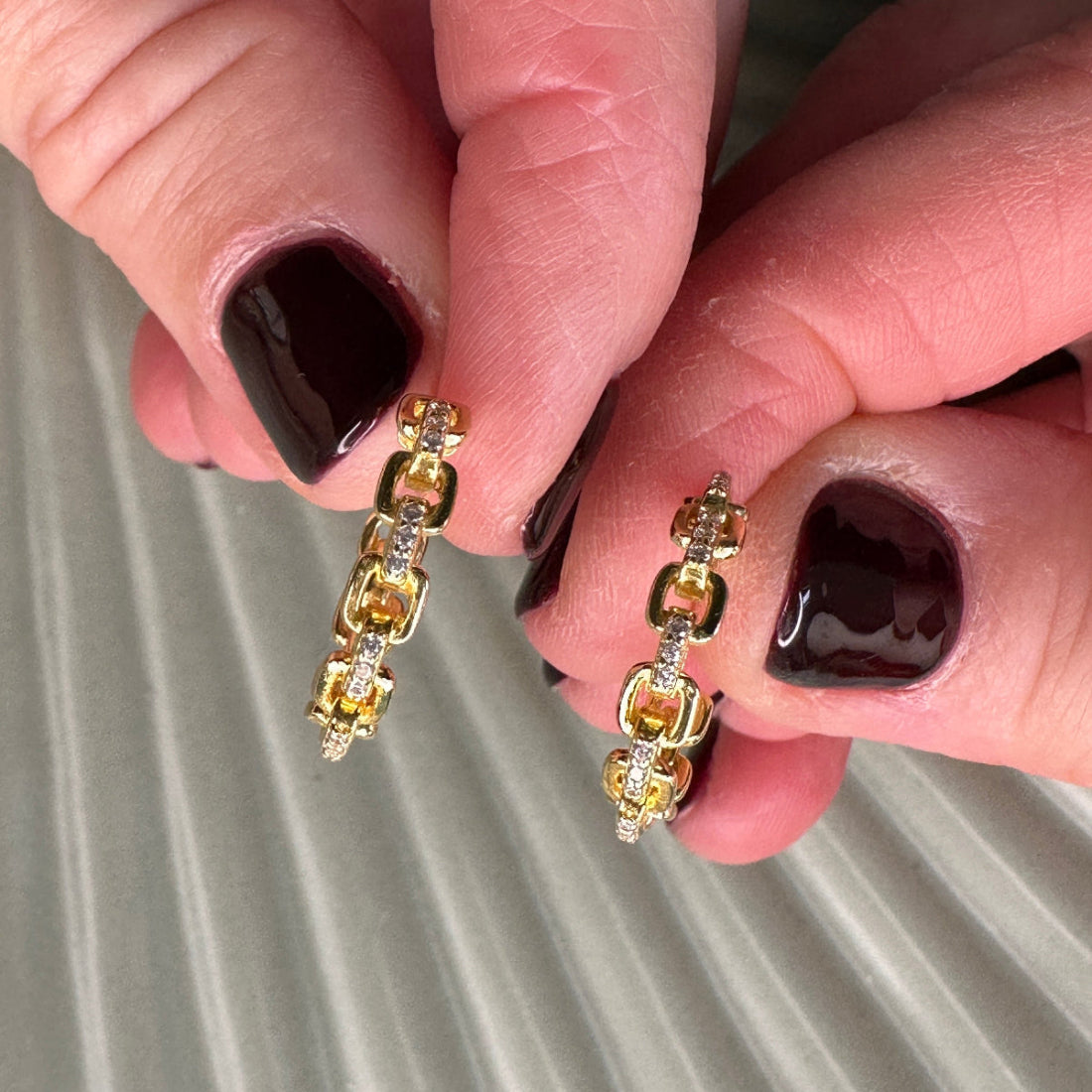 Gold hoop earrings with gemstones held between fingers against a neutral background