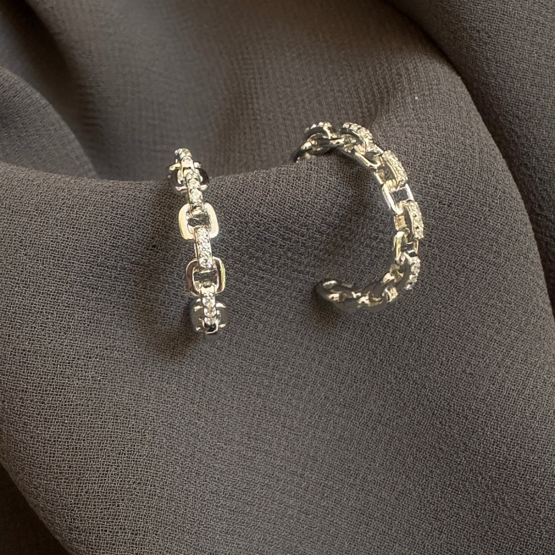 Pair of silver chain earrings on a dark fabric background