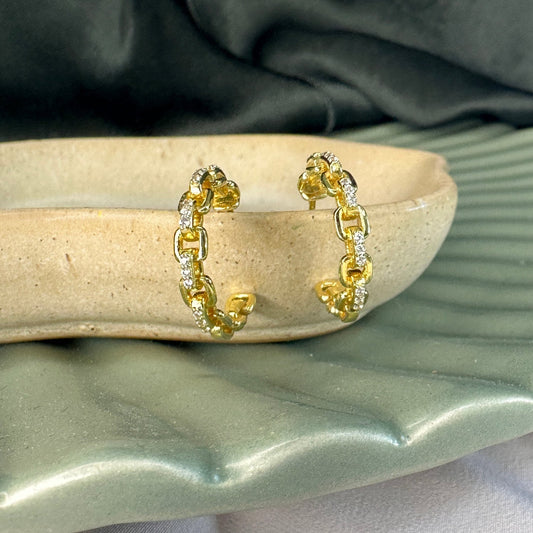 interlocking gold hoop earrign with gemstones on a cream dish