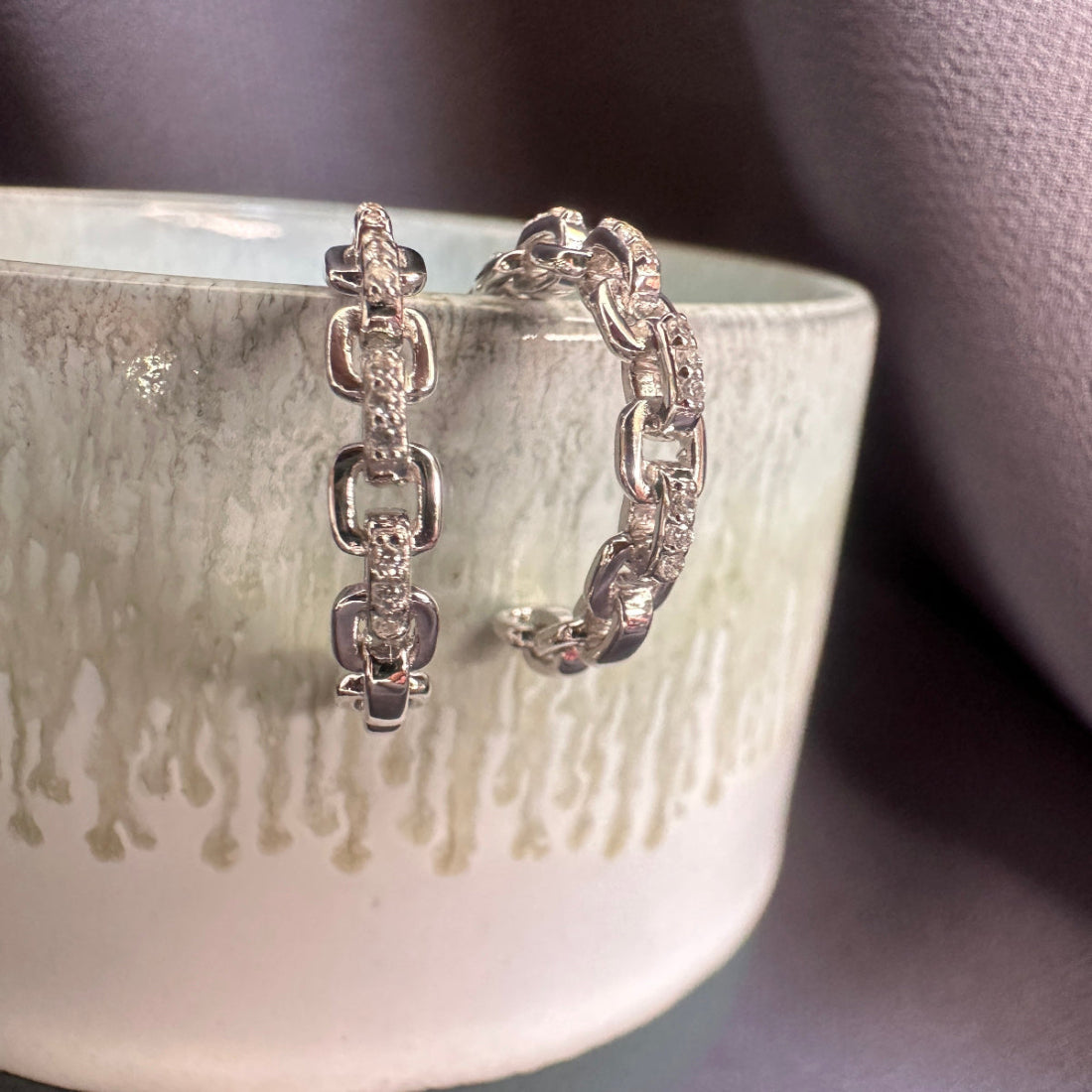 Silver interlocked link hoop earrings on a textured ceramic bowl