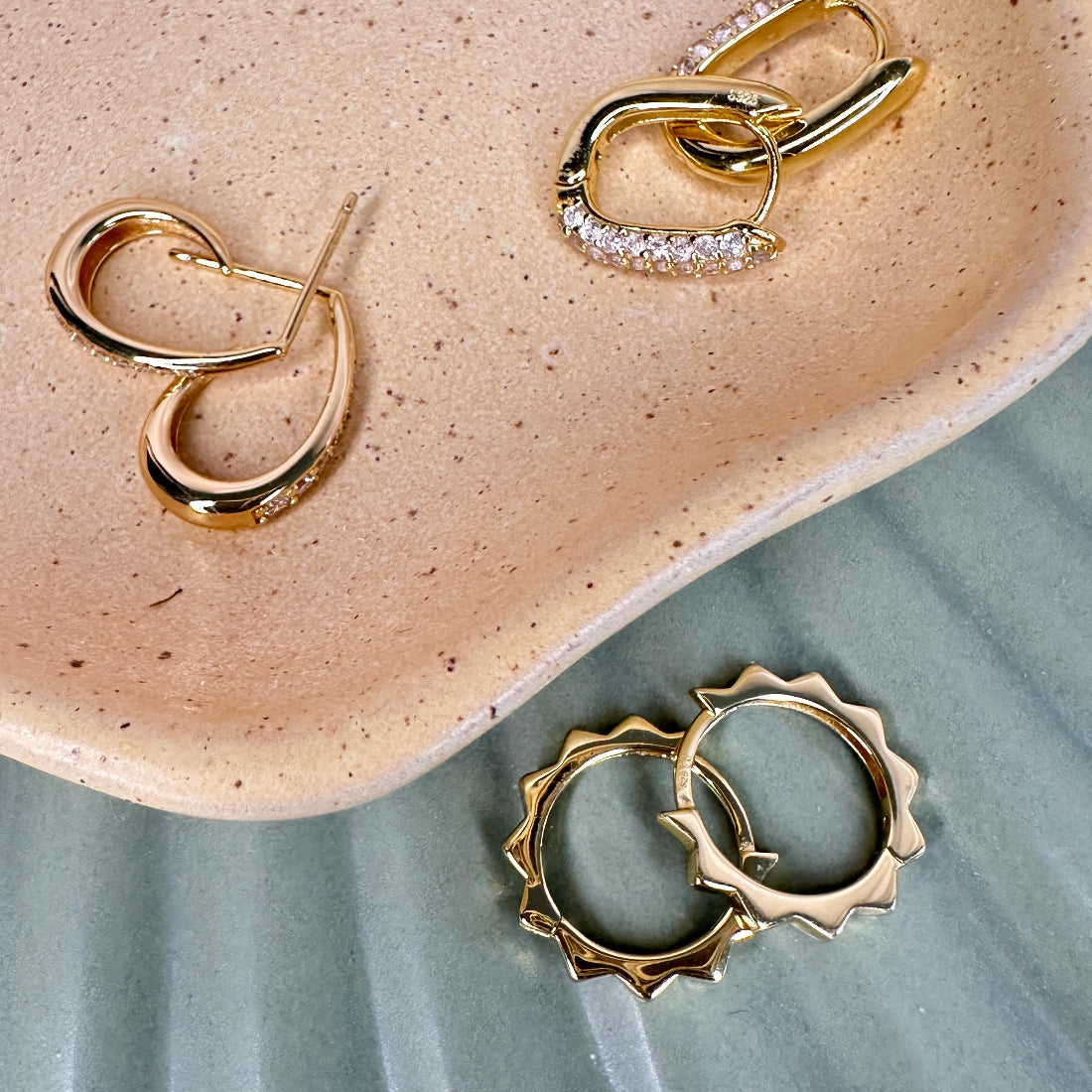 Trending gold hoop earrings with jagged edge detail on a textured surface