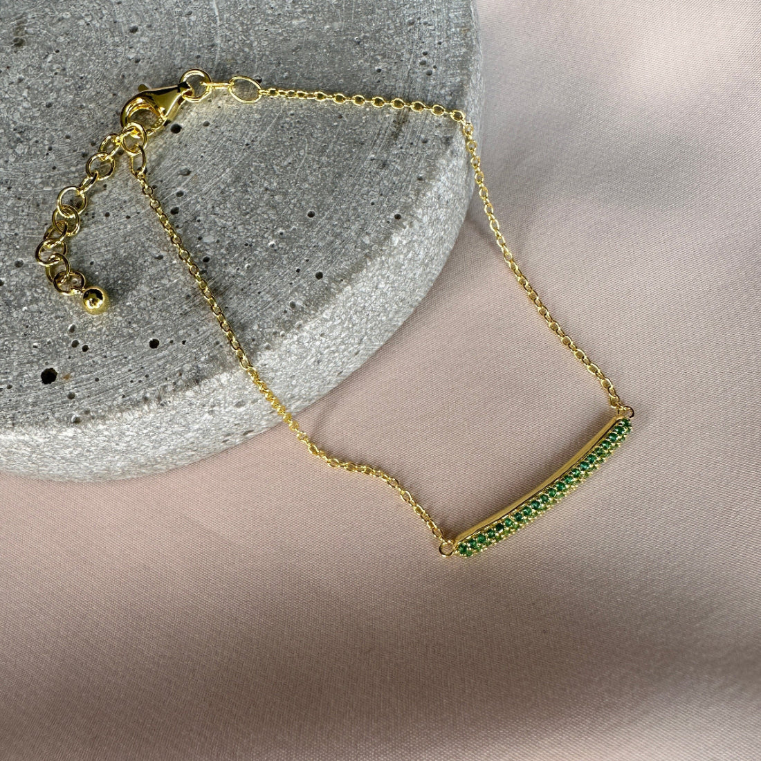 Gold bracelet with green stones on a neutral background