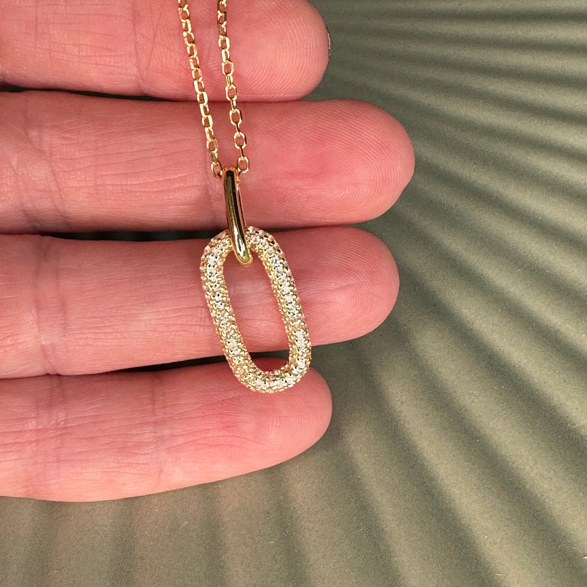 Gold necklace with a pendant held between fingers on a textured surface
