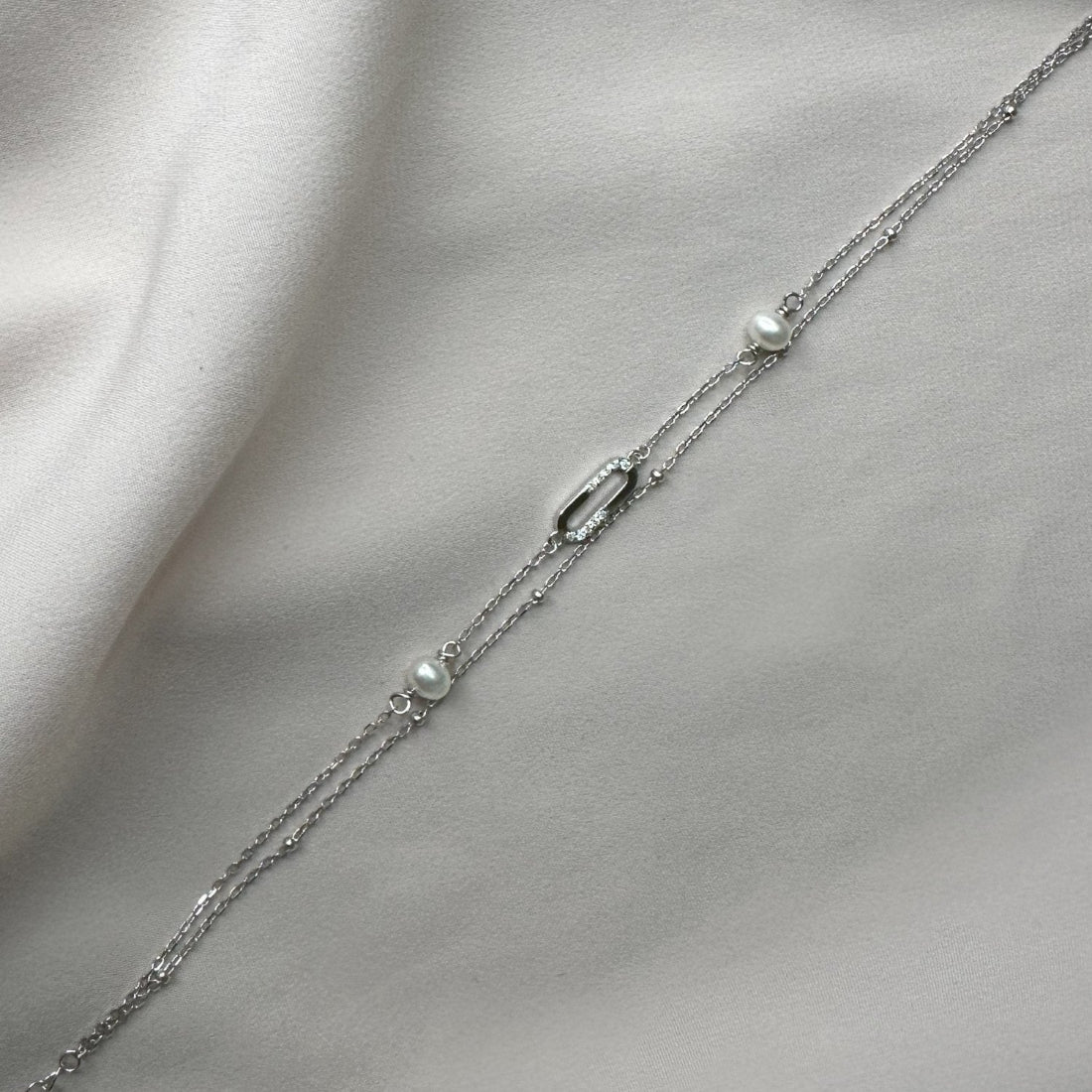 a doyble chain bracelet with 2 freshwater pearls and modern oval detail with gemstones laid on a pink ground