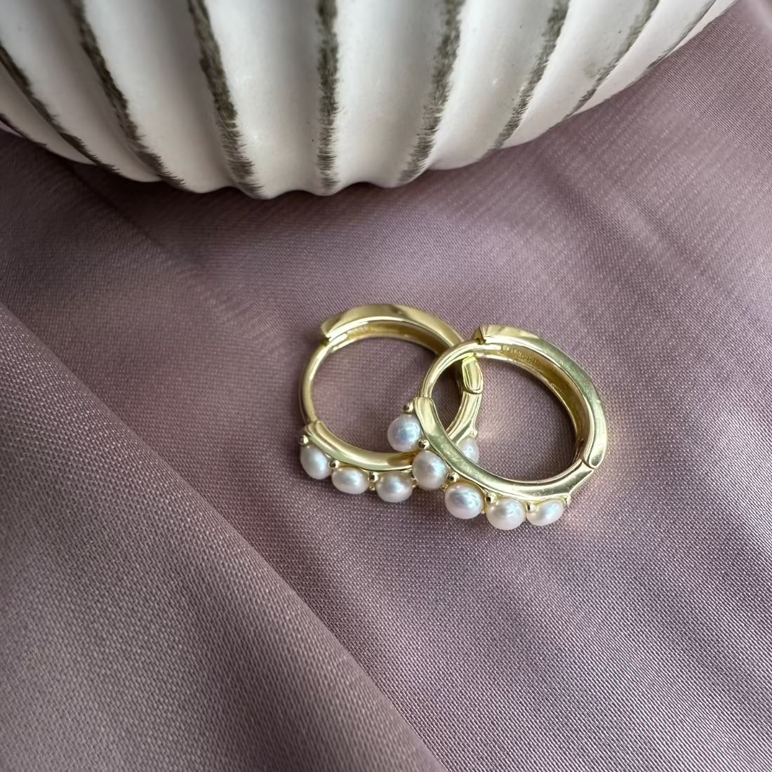 pair of gold hoops with freshwater pearls set in contemporary setting laid on pink gorund
