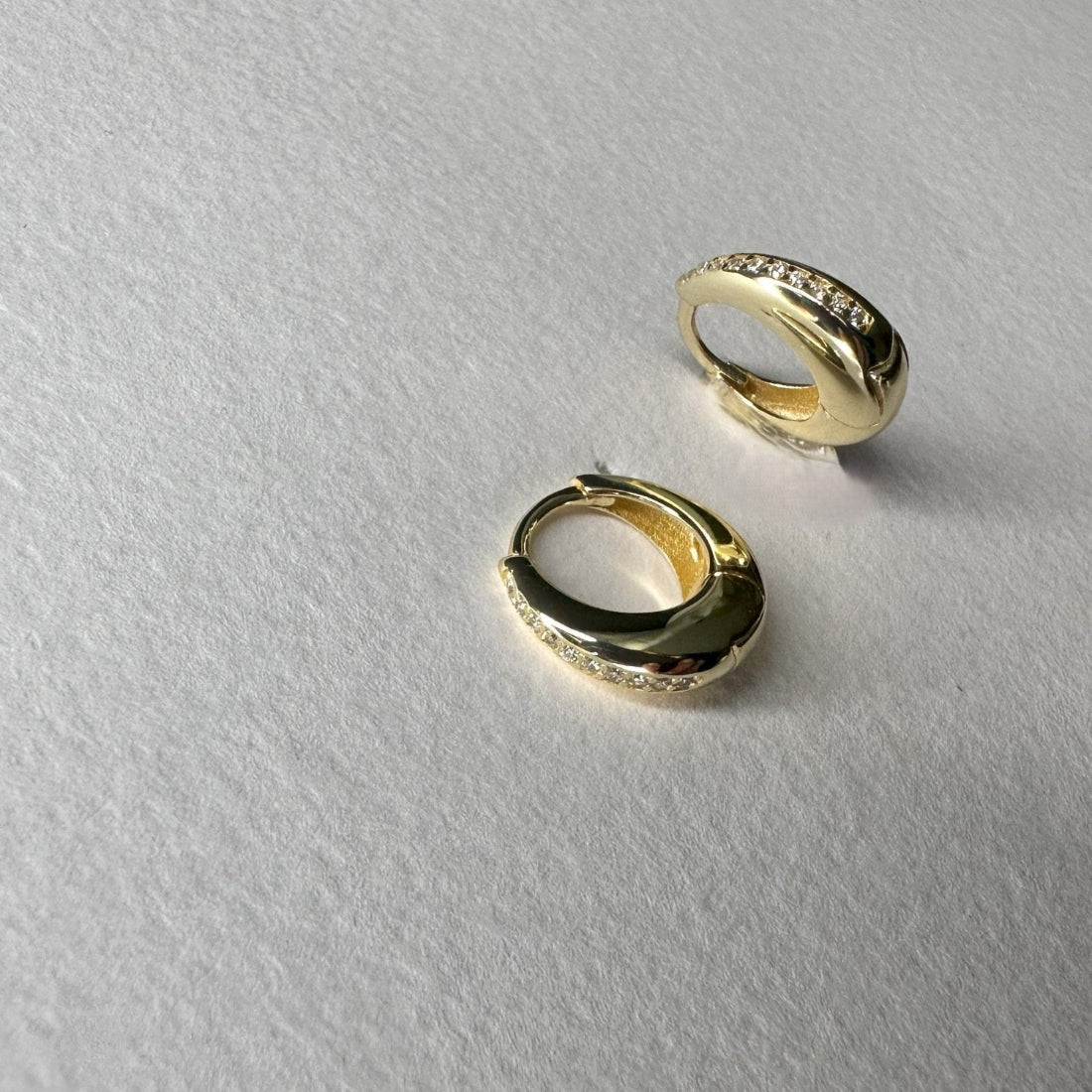 dome shaped gold huggies with gesmtones set in a channel setting laid on a white background