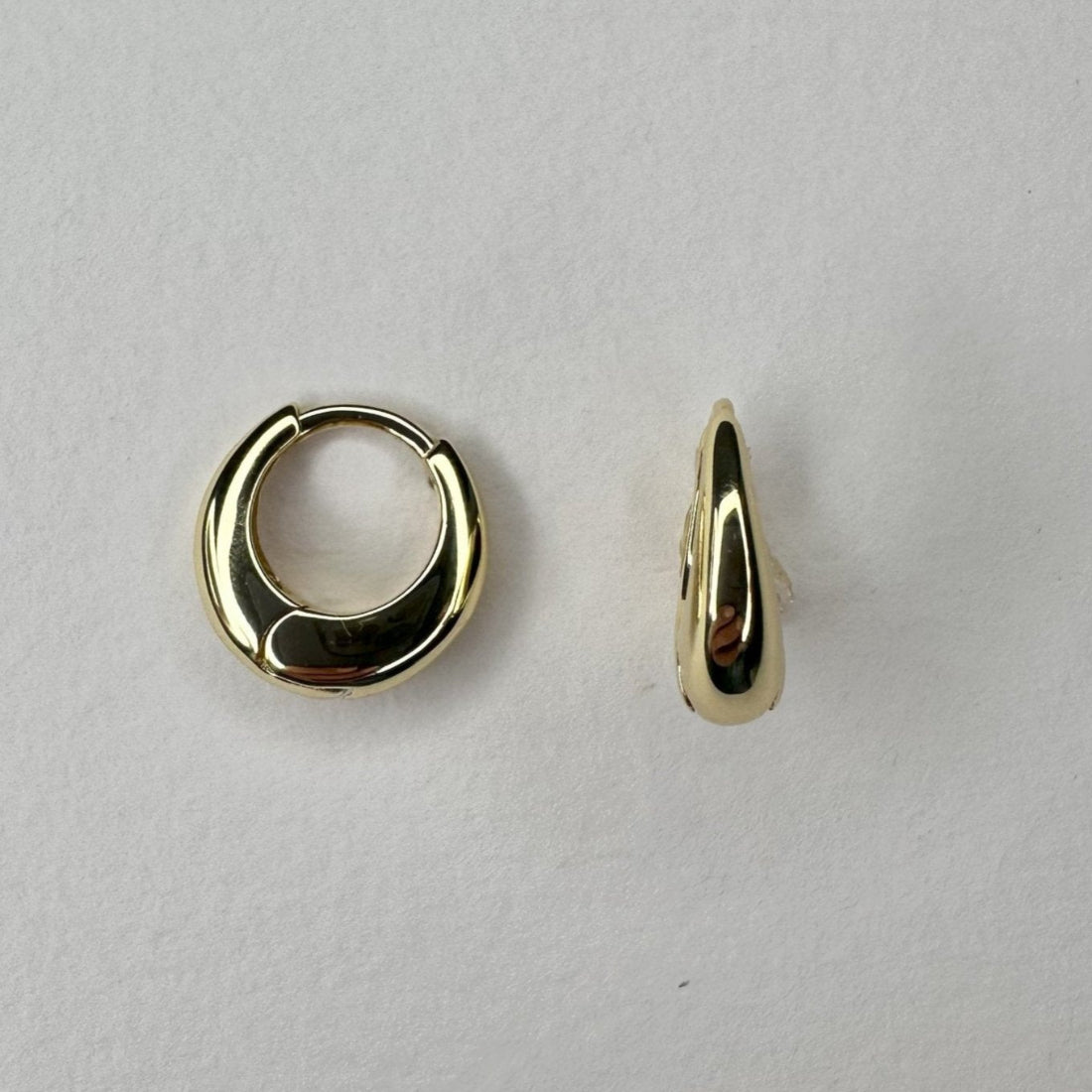 a pair of dome shaped huggie gold earrings laid on cream ground