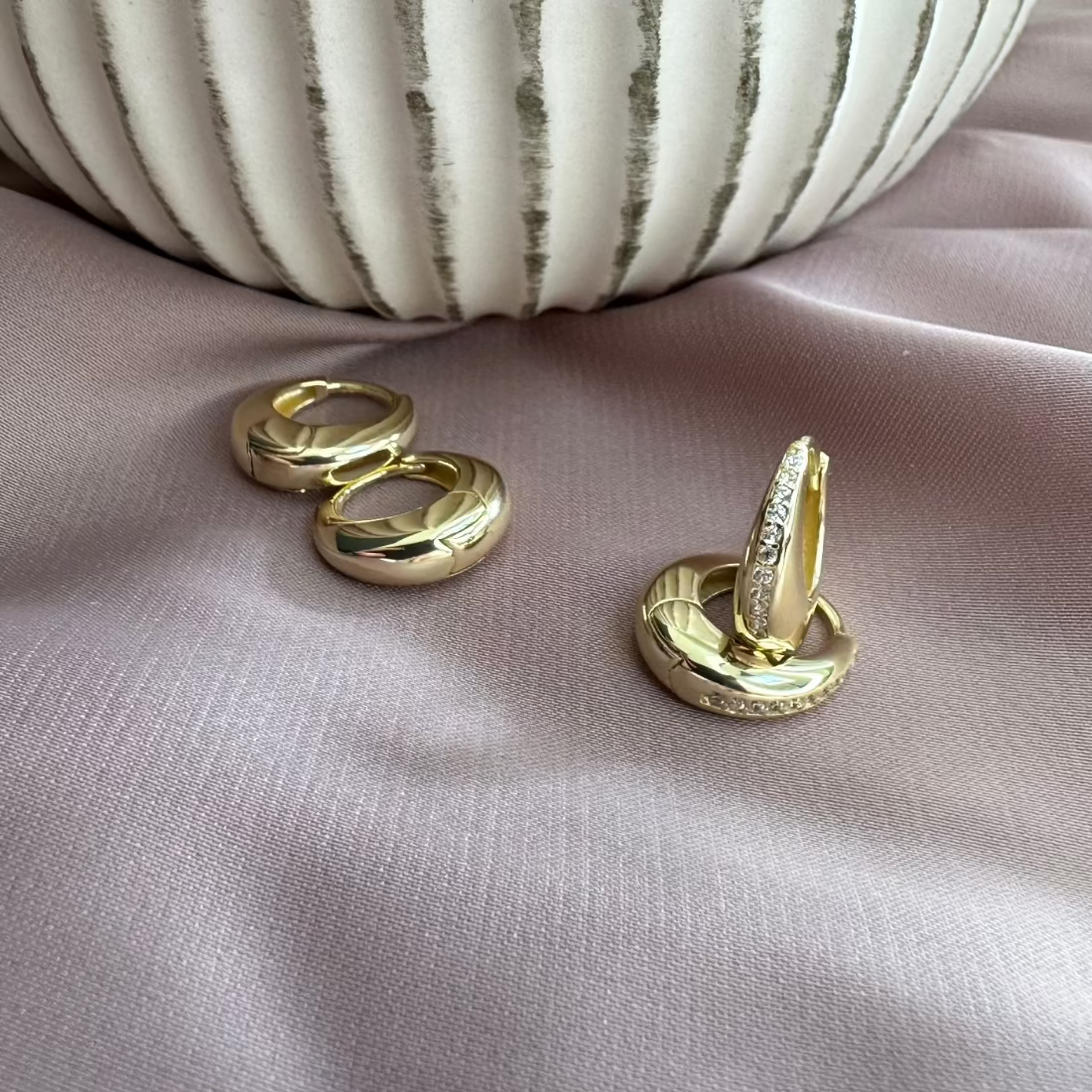 2 pairs of gold huggie earrings laid on blush ground