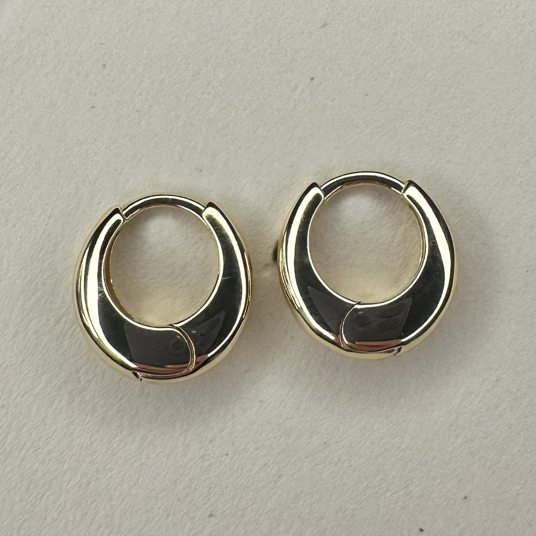 a pair of dome shaped huggie gold earrings laid on cream ground
