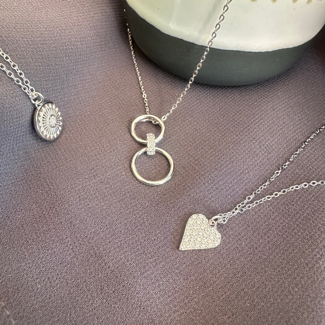 Three silver necklaces with unique pendants on a gray surface.