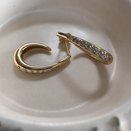 Gold hoop earring with embedded stones on a beige ceramic plate