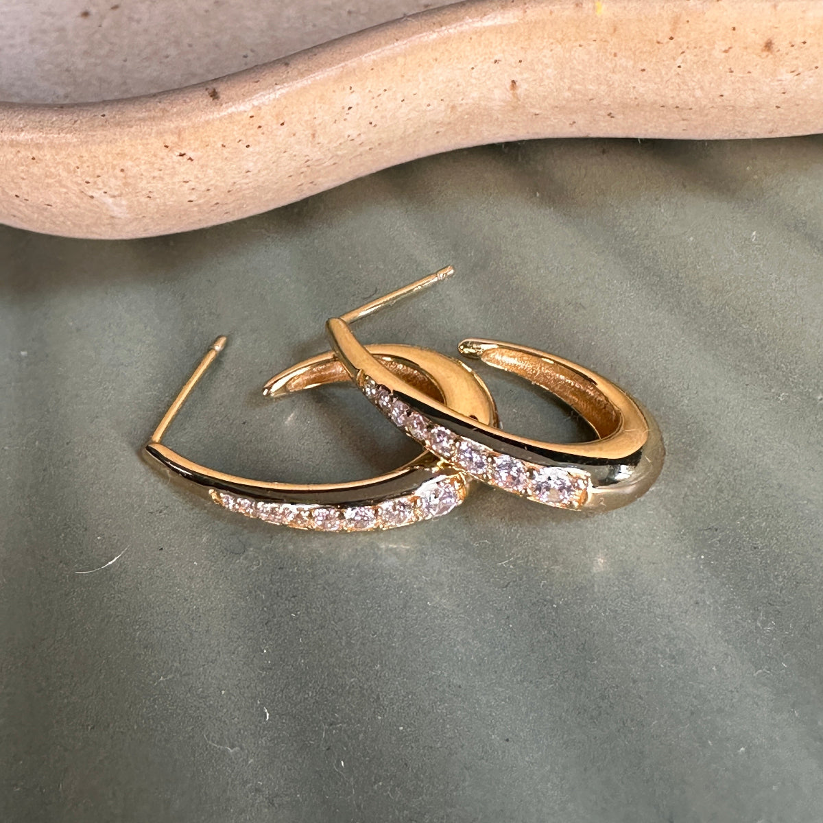 Gold hoop earrings with clear stones on a textured surface