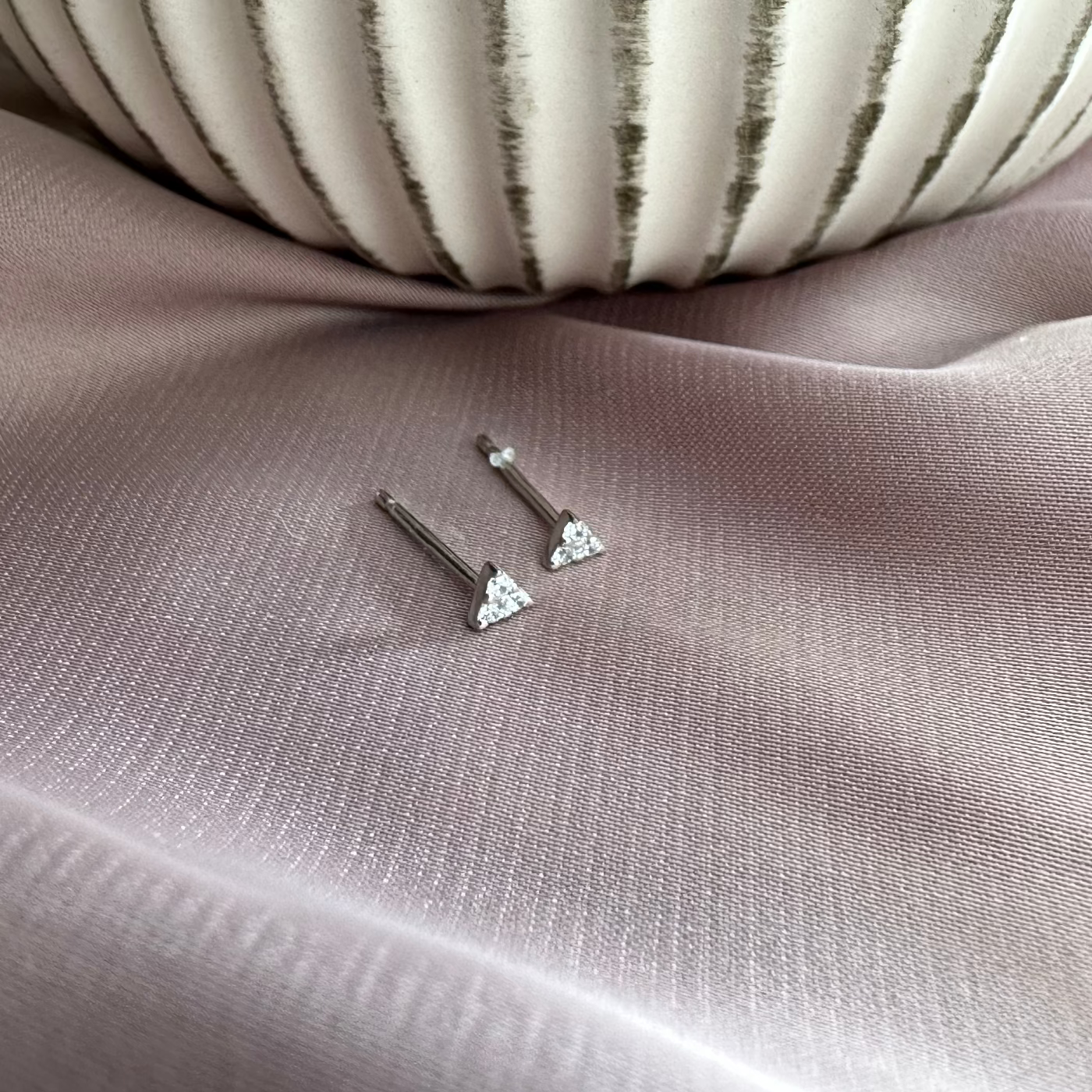 triangle mini stud earrings laid on pink surface