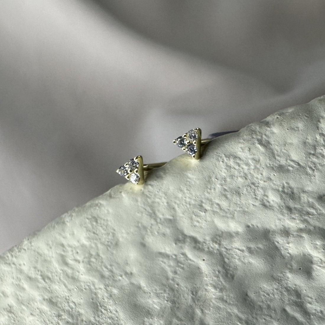 A pair of triangle-shaped gemstone earrings, with multiple sparkling stones, placed on a textured surface.