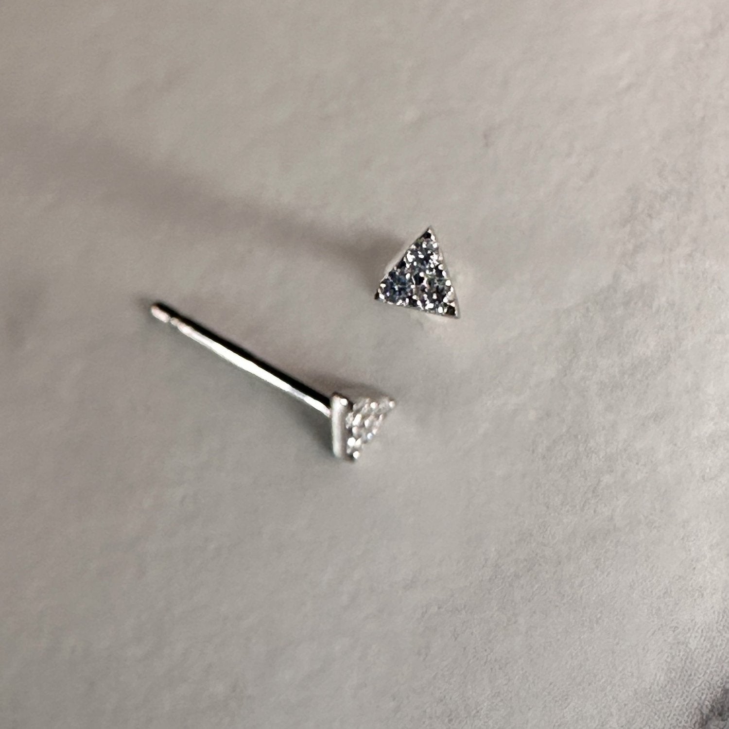 A pair of triangular gemstone stud earrings with a sparkling white faceted surface, displayed against a white background.