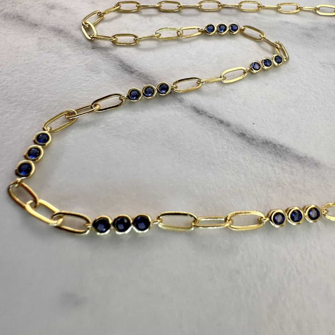 a close up image of a paperclip modern chain link necklace with triples of sapphire blue gemstones, laid on a white ground