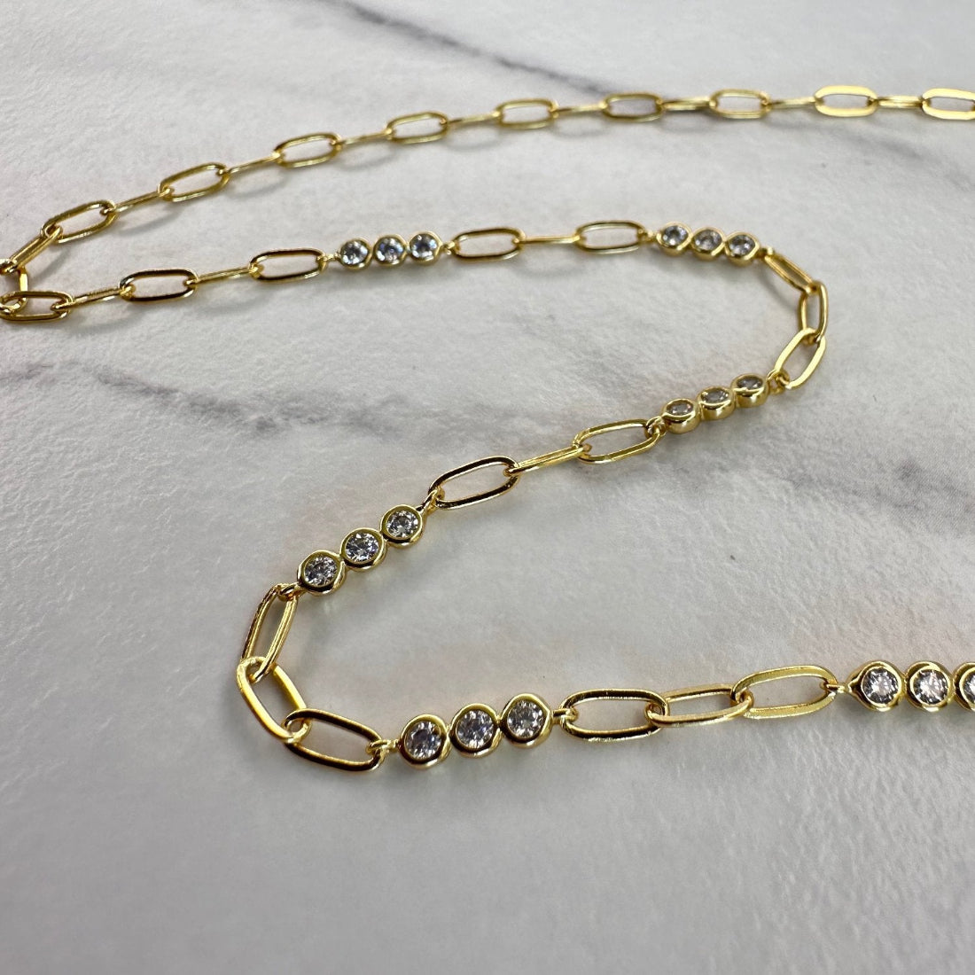 a close up image of a paperclip modern chain link necklace with triples of gemstones, laid on a white ground