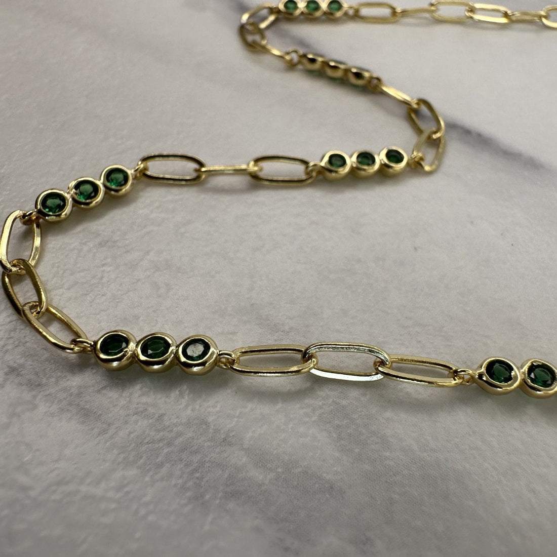 a close up image of a paperclip modern chain link necklace with triples of emerald green gemstones, laid on a white ground