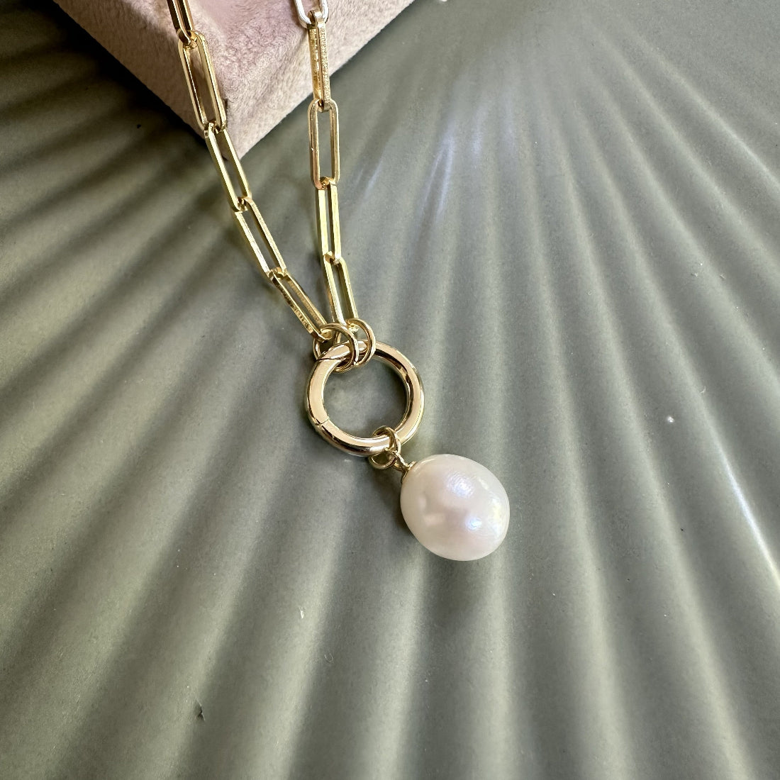 Statement Gold paperclip chain necklace with a natural freshwater pearl pendant charm on a textured surface