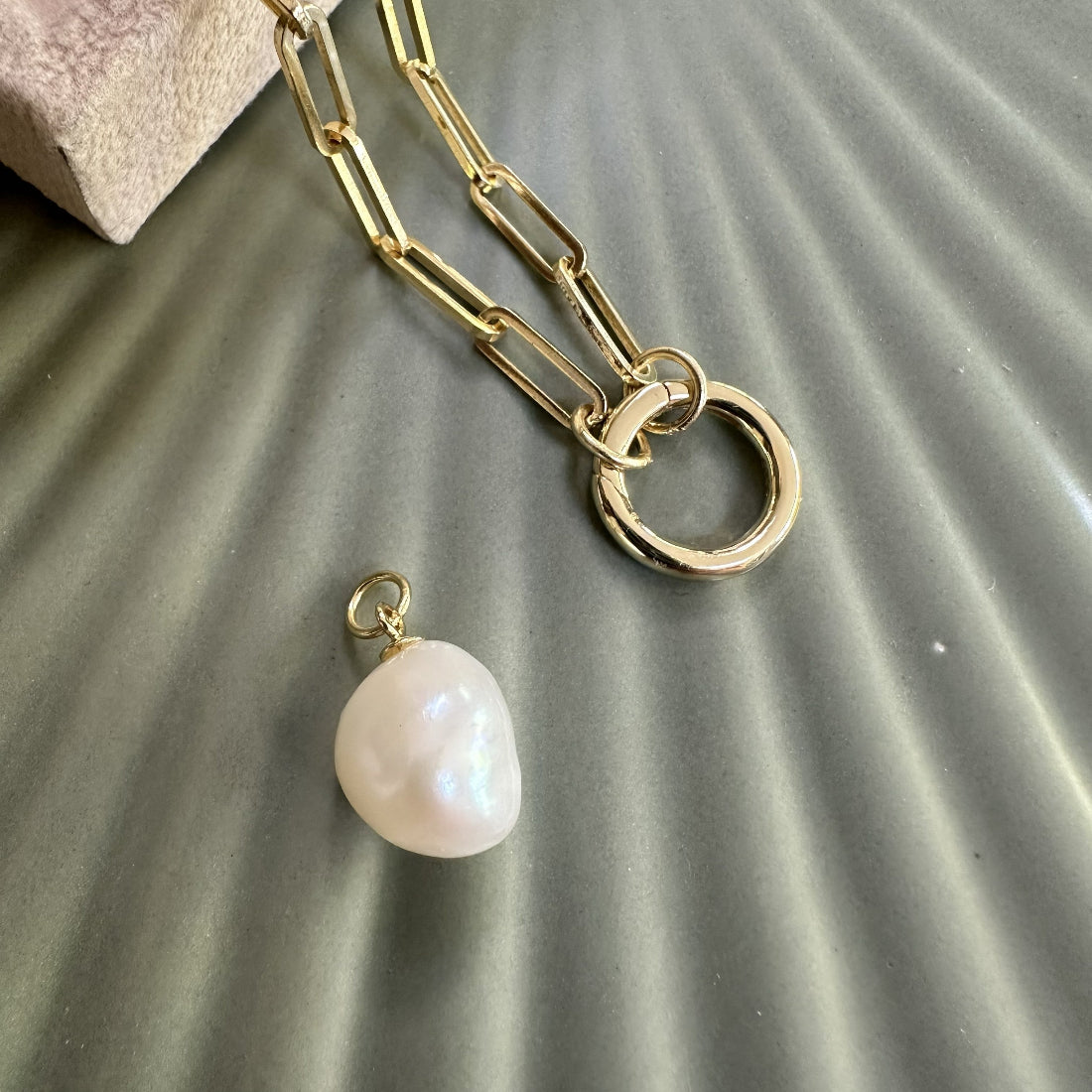 Gold chain necklace with a pearl pendant charm on a textured surface
