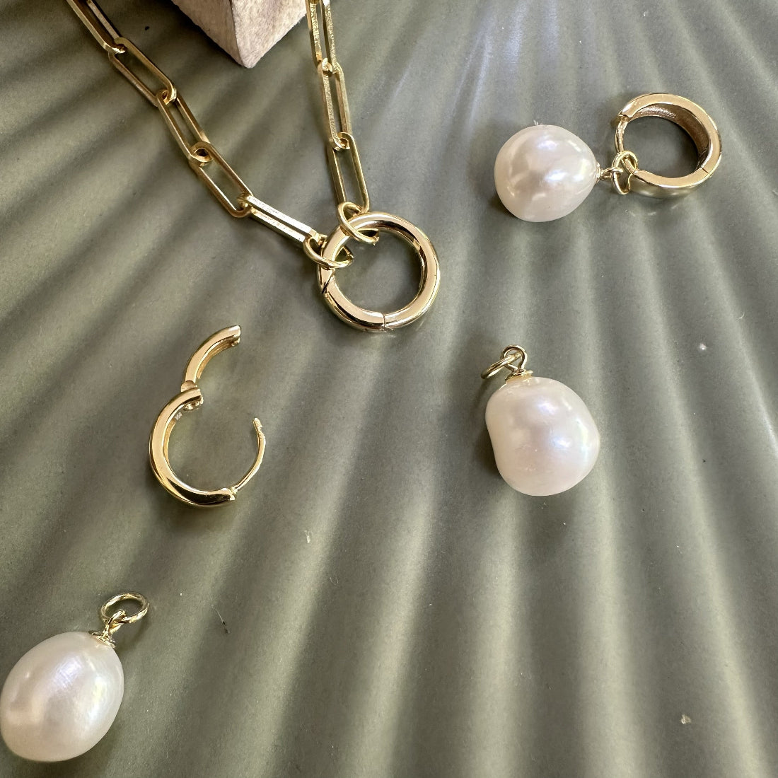 Gold jewelry set with natural freshwater pearl charm pendants with a statement paperclip chain necklace on a textured surface