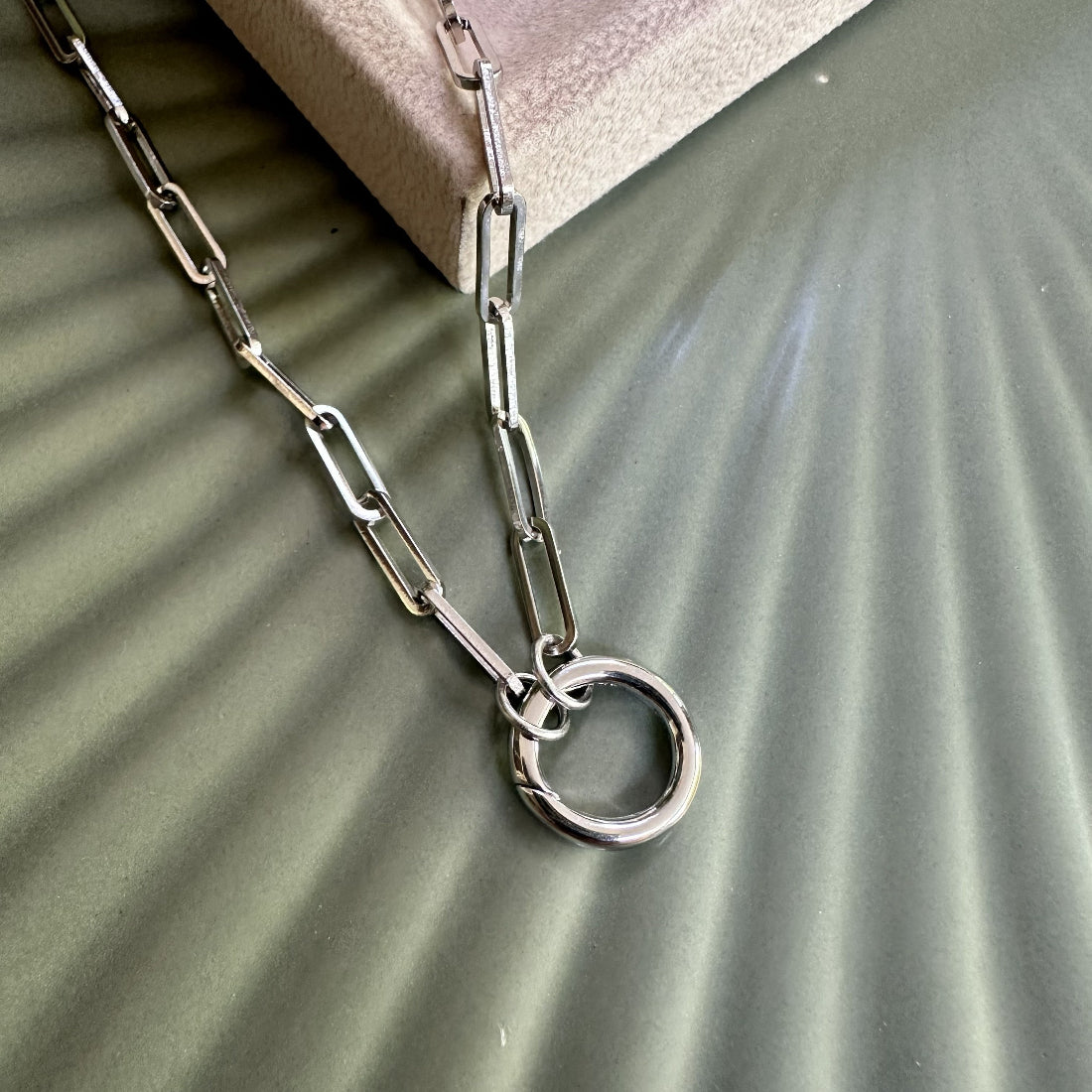 Silver statement paperclip chain necklace with a carabiner clasp for charm pendants on a green textured surface